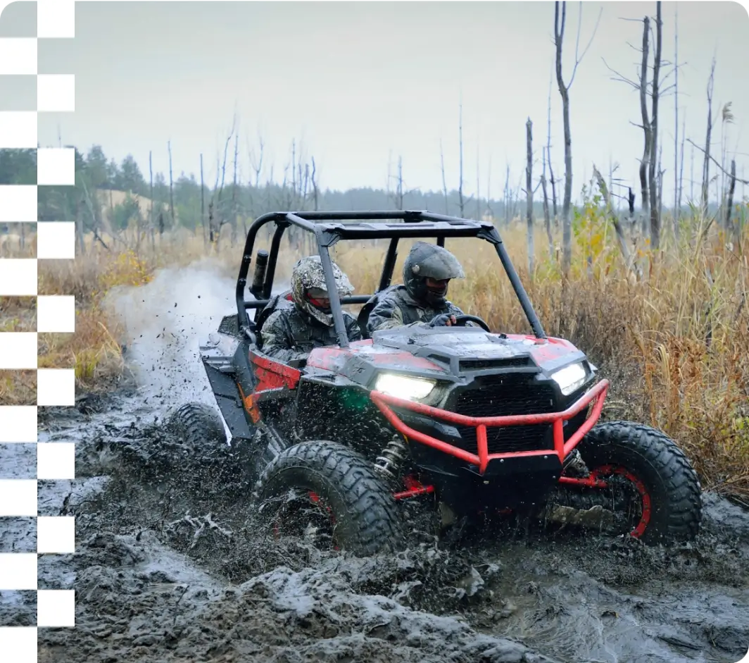 ATV driving through muddy terrain, forest backdrop.