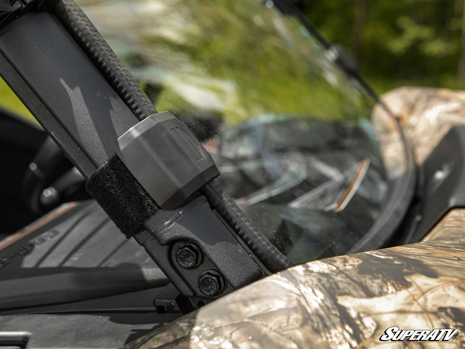 Close-up of a black tactical firearm accessory with a camouflage background.