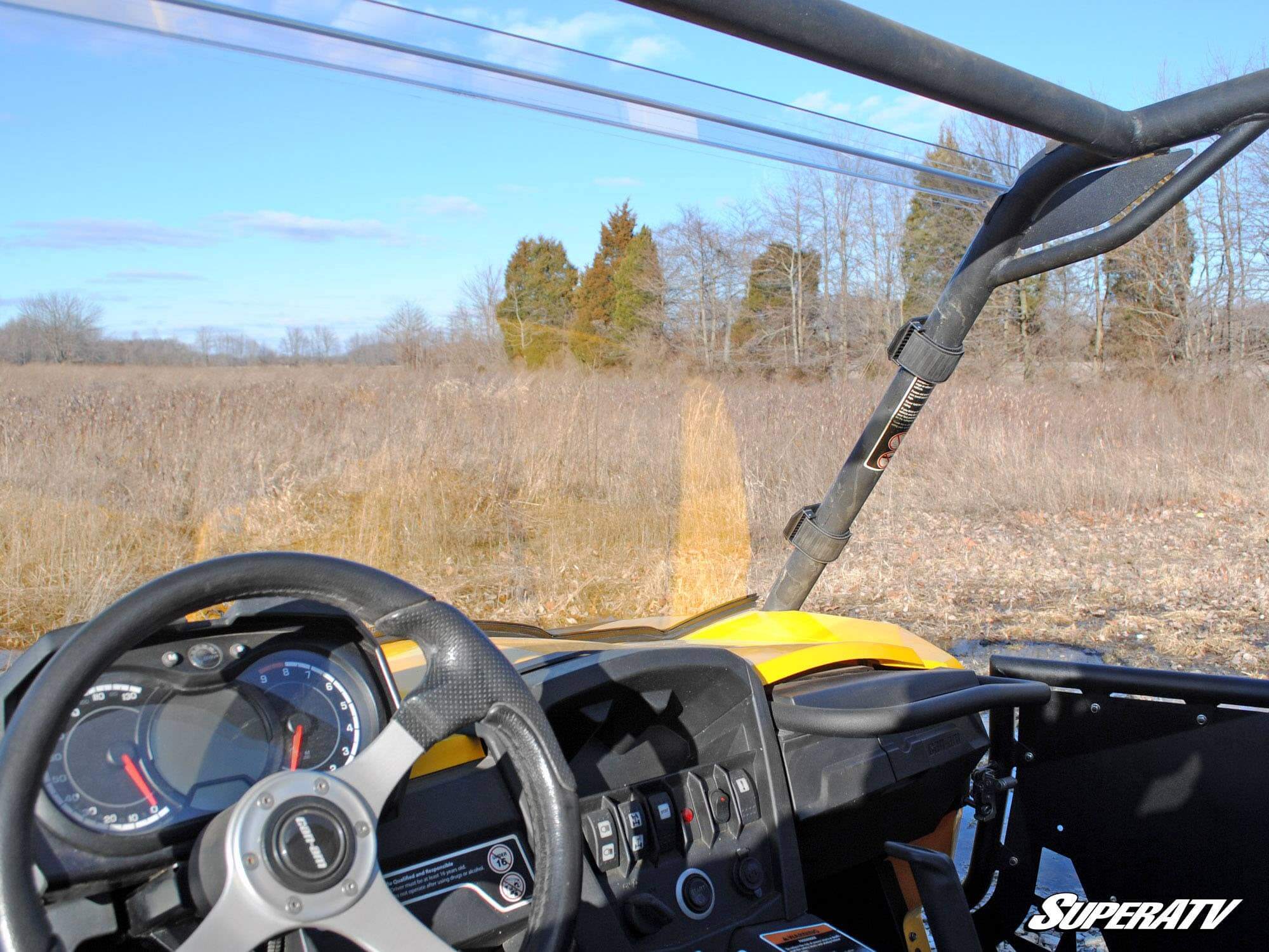 View from inside a yellow off-road vehicle overlooking a grassy field and trees.
