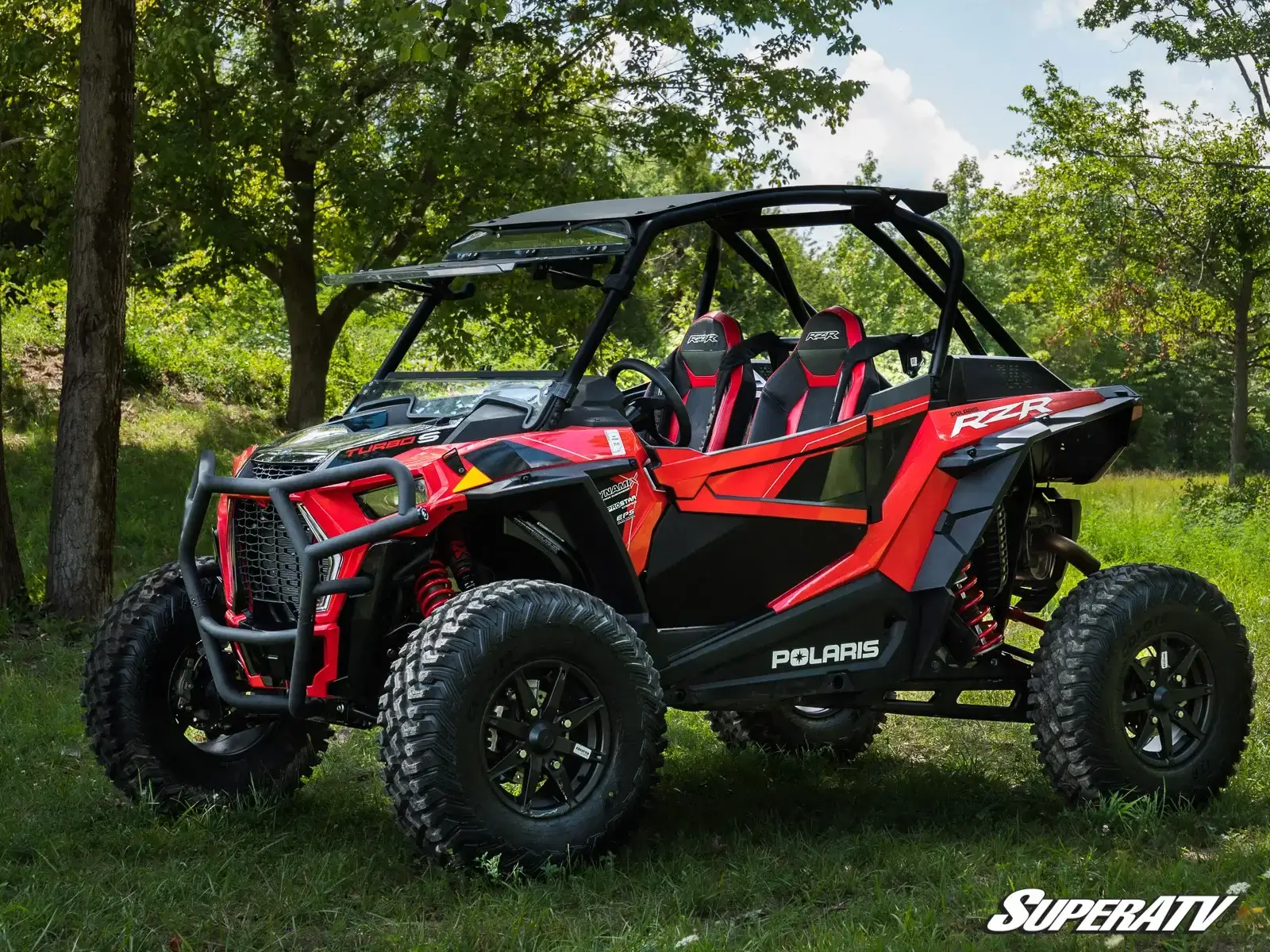 Red and black off-road Polaris vehicle parked outdoors under trees.