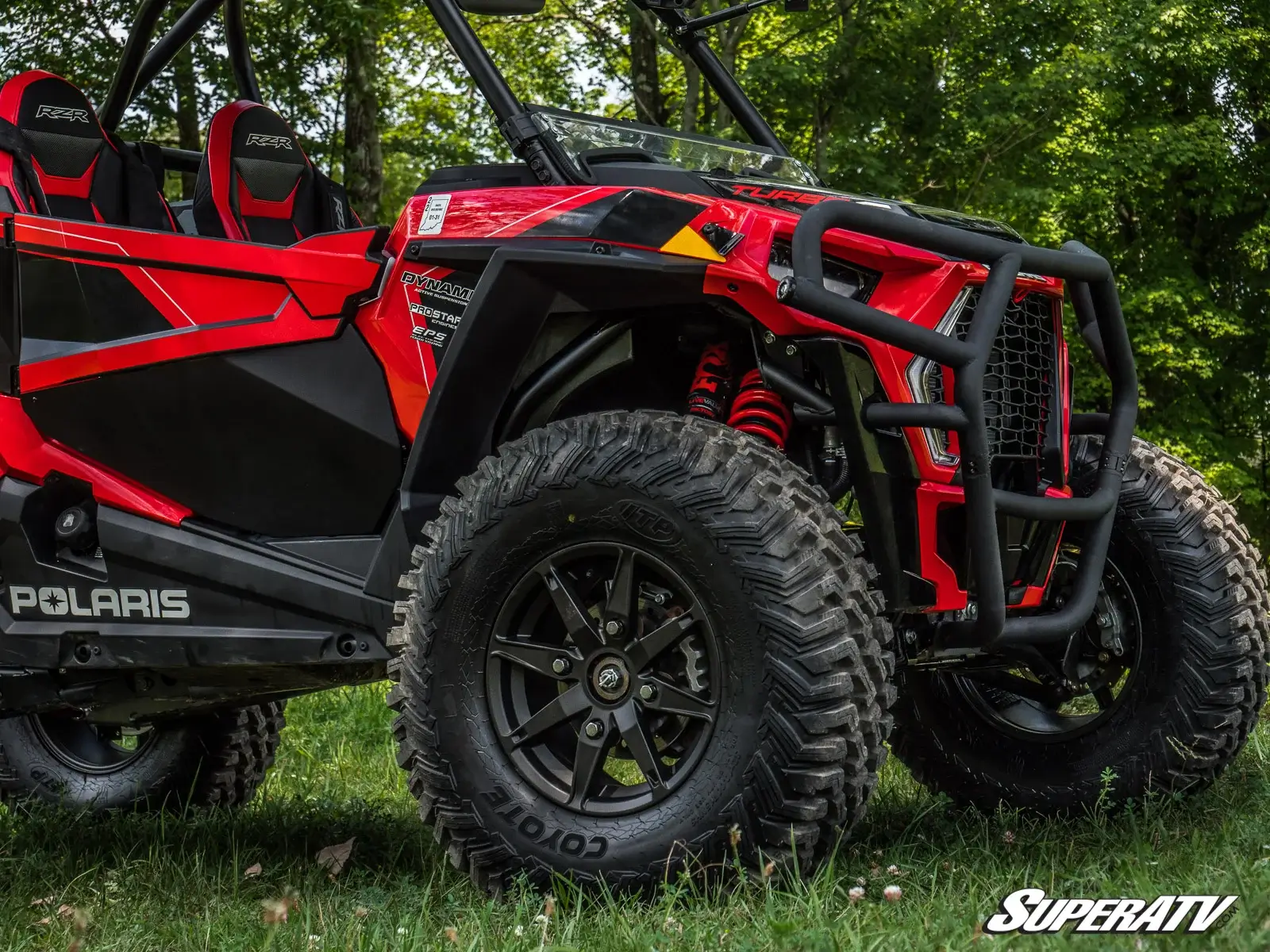 Close-up of a red off-road vehicle's rugged tire and front guard in a grassy area.